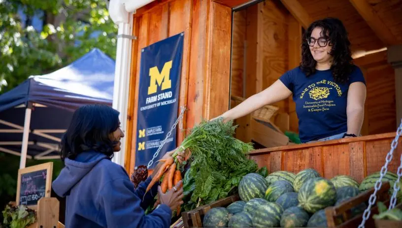 A student handing a person carrots at a campus farm stand