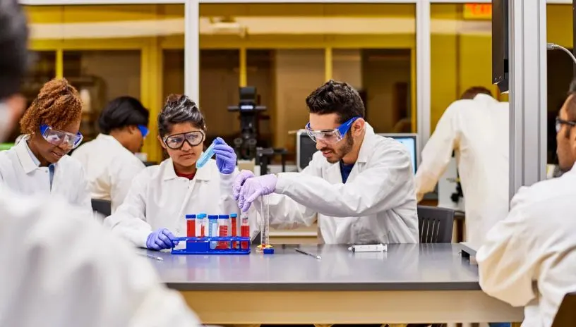 Researchers with lab gear looking at liquid in vials