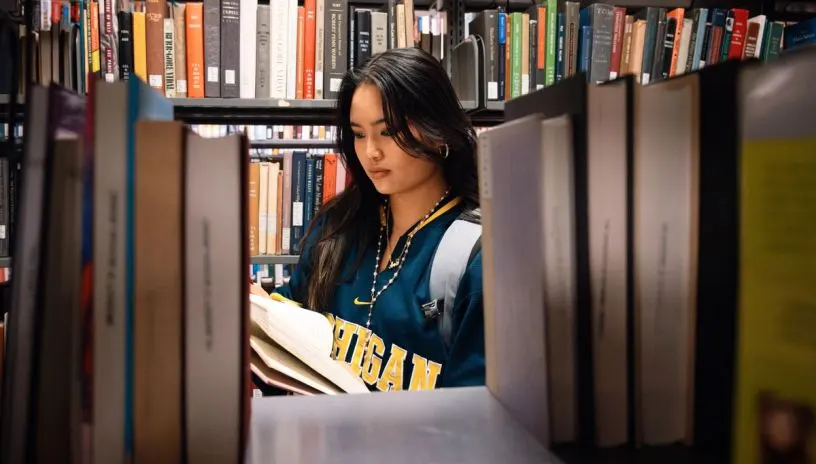A student reading a book in the stacks