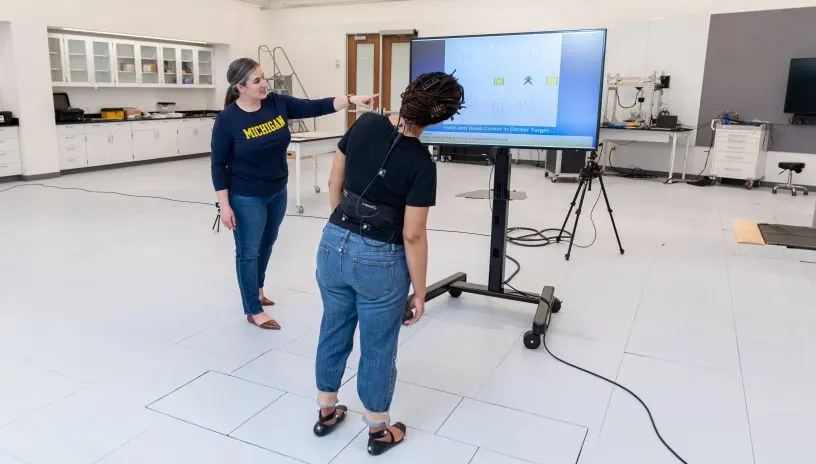 People standing and pointing at a large monitor in the middle of a room