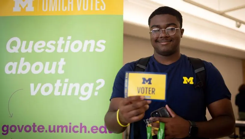 A smiling student leaving a Umich Votes center holding a Voter card